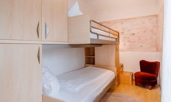 A bedroom with a bunk bed and a single bed. The room has bright wooden furniture and a cozy armchair.