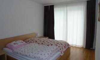 A bright bedroom with a large bed and colorful bed spreads. Bright curtains hang in front of the windows, letting in plenty of light.