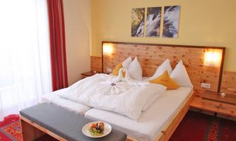 A cozy bedroom with a large double bed and bright walls. There is a fruit platter on a table, and the room is well-lit.