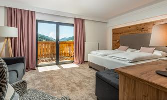 A modern hotel room with a large bed and a balcony. The room has large windows that offer a view of the mountains.