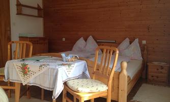 A simple room with wooden walls and a double bed. There are chairs at the table, and a placemat is lying on the table.