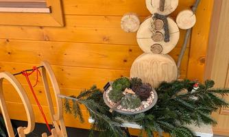 A wooden figure of a snowman stands against a wooden wall. Next to him lies a sled and a decorated tabletop with plants.