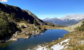A picturesque mountain lake surrounded by green meadows and mountains. The clear sky and the sun give the landscape a perfect ambiance.