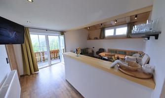 A modern living kitchen with wooden details and an open space concept. Large windows provide plenty of light and offer access to a balcony.