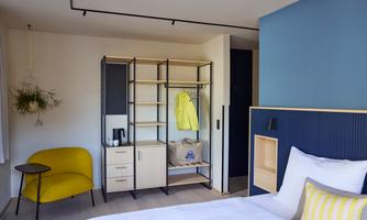 A modern bedroom with a cozy bed and a practical wardrobe. In the corner stands a yellow chair and the walls are designed in calming colors.