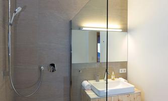 A modern bathroom with a shower and a washbasin. The walls are in neutral colors, and there is a large mirror wall.