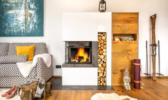 A stylishly furnished living room with a modern fireplace. The room features warm wood tones and cozy decorative elements.