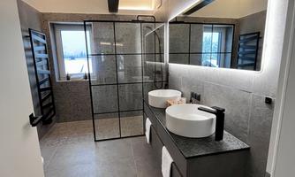 A modern bathroom with a large shower and double sinks. The walls are in neutral colors and the lighting creates a pleasant atmosphere.