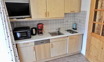 A modern kitchen unit with wooden cabinets and a small refrigerator. There is a sink, a stove, and various kitchen appliances.