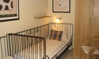 A cozy children's room with two crib beds and soft lighting. Pictures hang on the wall, and a wicker chair is in the corner.