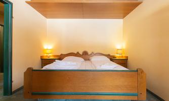 A bedroom with a large, rustic wooden bed and two nightstands. The walls are in soft colors and the lighting creates a cozy atmosphere.