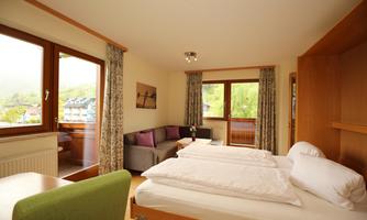 A bright room with two beds, a sofa, and large windows. The furnishings are modern and friendly.
