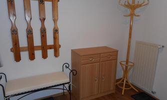 A cozy hallway with a wooden bench, a shoe cabinet, and a coat rack. Coat hooks are attached to the wall.