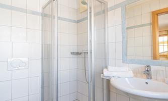 A modern bathroom with a shower cabin and a sink. Bright tiles and simple furnishings create a clear atmosphere.