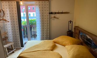 A cozy bedroom with a double bed and yellow cushions. The windows offer a view of a balcony and the surrounding landscape.