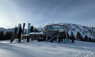 A modern ski building in a snowy landscape. In the background, mountains and coniferous trees can be seen.