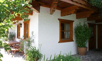 A cozy house with white walls and wooden decorations. The outdoor area is green with many plants and tables for relaxing.