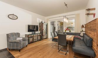 A modern living room with a dining table and a cozy corner. Large windows provide plenty of daylight.