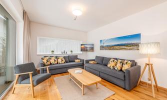 A modern living room with two comfortable sofas and a wooden coffee table. The large windows let in plenty of light and create a bright atmosphere.