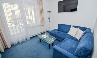 A cozy living room with a blue sofa and a glass table. Large windows let in a lot of light.