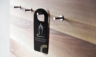A black sign with the inscription "MEDITATING" hangs on a wooden surface. The sign requests not to be disturbed.