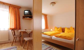 A cozy room with two beds and yellow cushions. A small sitting area with a table and a TV is also visible.
