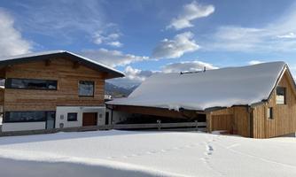 A modern wooden house in the snow under a clear blue sky. The surrounding landscape is covered with fresh, white snow.