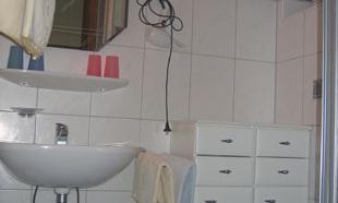A small bathroom with a sink, a mirror, and a chair. The walls are tiled and the decor is simple.