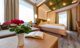 A cozy room with a large bed and soft colors. On the table is a flower vase and an open book.