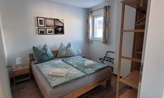 A cozy bedroom with a double bed and two pillows. The walls are light, and there is a small table as well as decorative pictures.