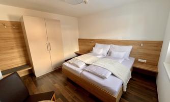 A modern bedroom with a large double bed and bright wood interior. Additionally, there is a table and a chair as well as a wardrobe.