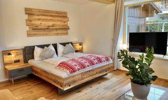 A modern bedroom with a cozy double bed and wooden furniture. Large windows provide plenty of daylight and a pleasant atmosphere.