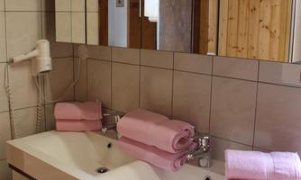 A modern bathroom with a double sink and a large mirror. Pink towels are neatly arranged on the countertop.