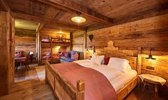 A cozy wooden room with two beds and warm light. The furnishings create a rustic and inviting atmosphere.