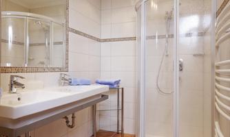 A modern bathroom with a shower and a large mirror. On the sink are two blue towels.