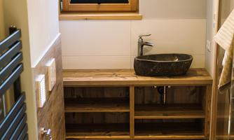 A modern bathroom with a window offering a view of the mountains. There is a stylish sink and a wooden shelf.