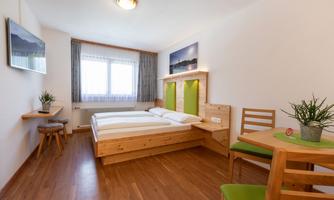 A modern bedroom with two single beds and a wooden design. There is a small dining table and plenty of daylight through the windows.