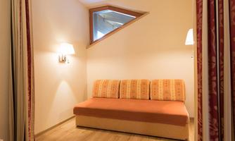 A cozy room with a colorful sofa and soft light. The walls are bright, and there is a striking window in triangular shape.