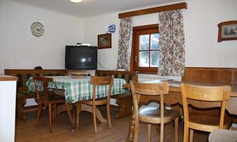 A cozy dining area with wooden tables and chairs. A television and windows with curtains give the room an inviting atmosphere.