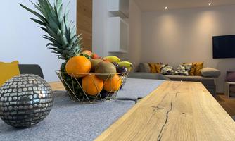 A stylish living room with a wooden tabletop and a fruit bowl full of colorful fruits. In the background, cozy sofas and a television are visible.