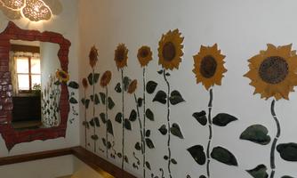 A wall with colorful sunflowers, artfully painted. In the corner hangs a decorative mirror.