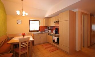 A cozy kitchen with wooden cabinets and a seating area. The room has a bright atmosphere with natural light.