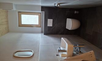A modern bathroom with a small sink and a toilet. Light comes through a window, and the walls are painted in neutral colors.