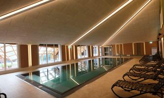 A modern indoor pool with large windows and elegant lighting.  
Comfortable loungers are positioned along the pool.