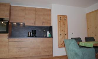 A modern kitchen with wooden cabinets and a black countertop. On the right, there is a dining table with green chairs.