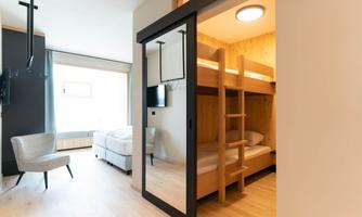 A modern hotel room with a single bed and a loft bed. The room feels bright and friendly with minimalist decor.