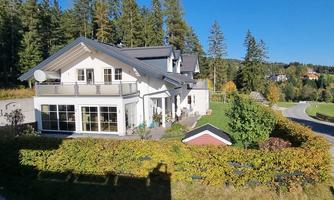 A beautiful house surrounded by trees and a well-maintained garden. The sky is clear and the surroundings feel calm and inviting.