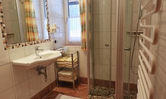 A modern bathroom with a shower and a sink. Towels are neatly stacked and the window provides natural light.