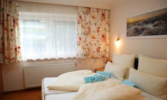 A cozy bedroom with two beds and colorful curtains. The window lets in plenty of daylight and creates a friendly atmosphere.
