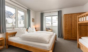 A cozy bedroom with two beds and a wooden bunk bed. Large windows offer a wonderful view of the mountains.